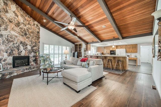 living area with a stone fireplace, beamed ceiling, and dark wood finished floors