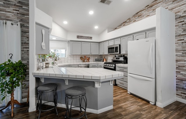 kitchen with appliances with stainless steel finishes, a peninsula, decorative backsplash, tile countertops, and a breakfast bar area