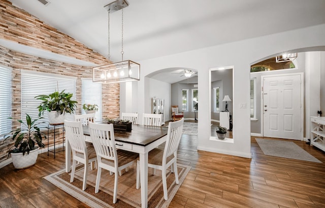 dining room featuring arched walkways, wood finished floors, ceiling fan, high vaulted ceiling, and baseboards