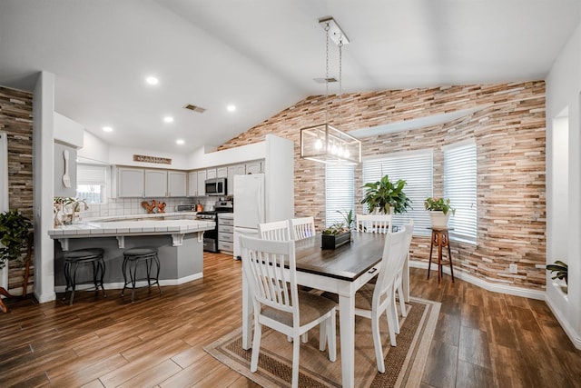 dining space featuring wood finished floors, lofted ceiling, and brick wall