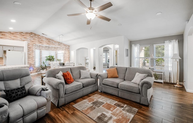 living room featuring vaulted ceiling, arched walkways, a ceiling fan, dark wood-style flooring, and brick wall