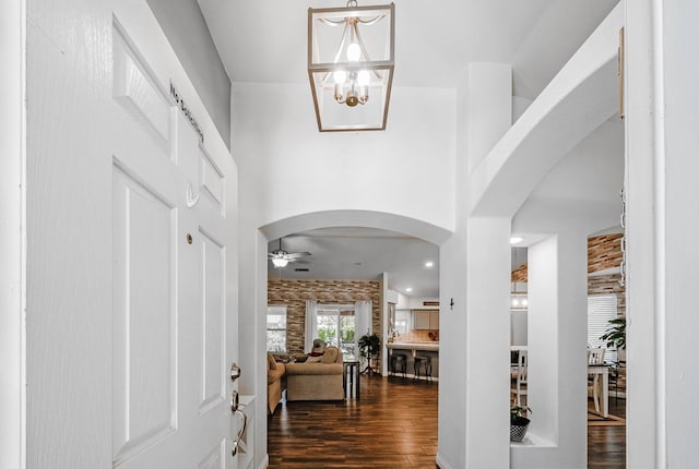 foyer entrance with arched walkways, dark wood-style flooring, ceiling fan, a chandelier, and a high ceiling