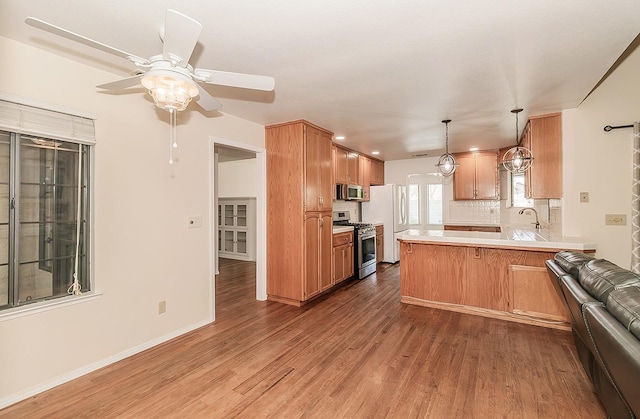 kitchen featuring stainless steel appliances, a peninsula, a ceiling fan, wood finished floors, and light countertops