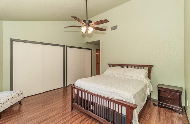 bedroom with vaulted ceiling, visible vents, a ceiling fan, wood finished floors, and two closets