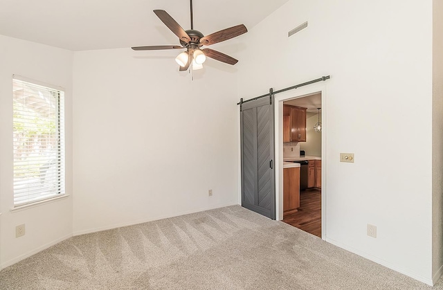 unfurnished room with a ceiling fan, visible vents, dark carpet, and a barn door