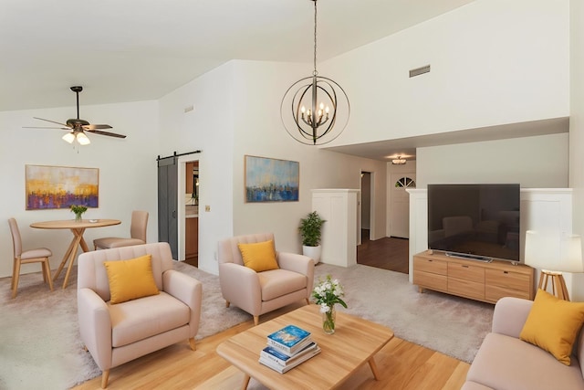 living room with high vaulted ceiling, a barn door, ceiling fan with notable chandelier, light wood-style flooring, and visible vents