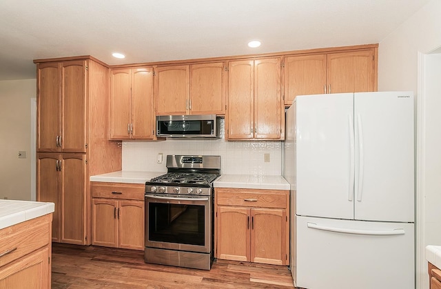 kitchen featuring backsplash, wood finished floors, tile countertops, and stainless steel appliances