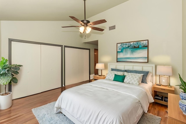 bedroom with visible vents, lofted ceiling, a ceiling fan, wood finished floors, and multiple closets