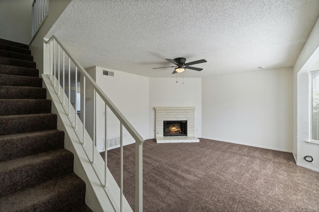 unfurnished living room featuring ceiling fan, visible vents, carpet floors, stairway, and a brick fireplace