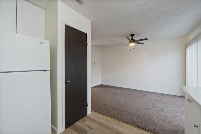 kitchen featuring baseboards, freestanding refrigerator, a ceiling fan, white cabinetry, and light carpet