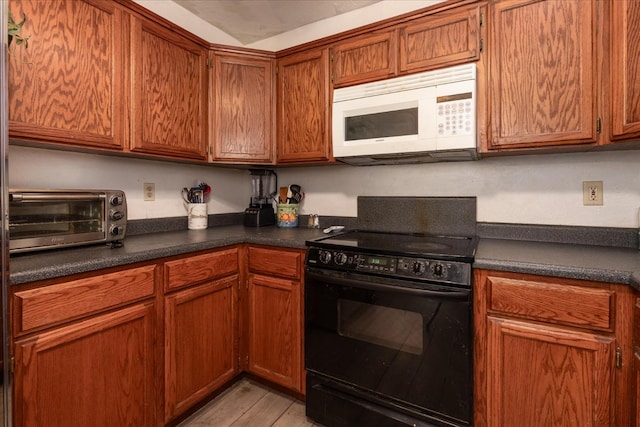 kitchen featuring dark countertops, black electric range oven, brown cabinets, white microwave, and a toaster