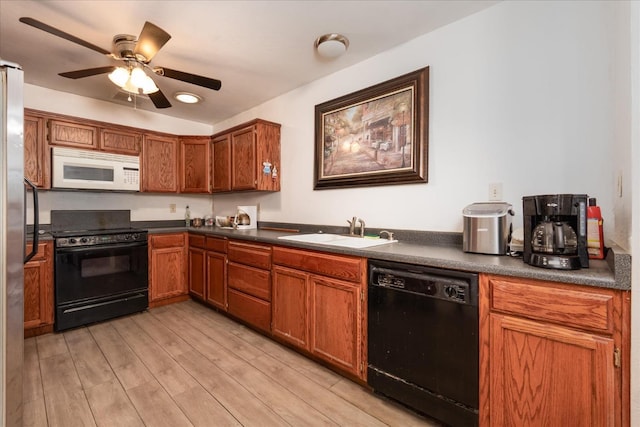 kitchen with light wood-style floors, a ceiling fan, black appliances, a sink, and dark countertops