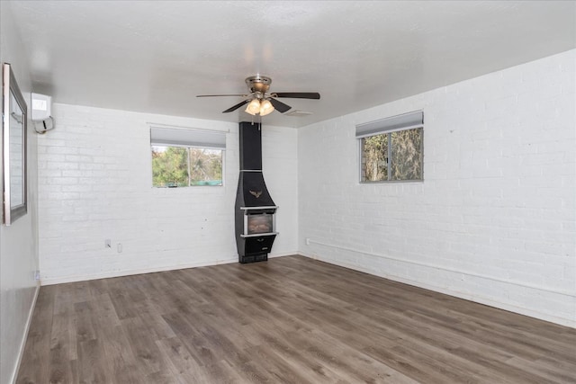 unfurnished living room with visible vents, brick wall, a wood stove, ceiling fan, and wood finished floors