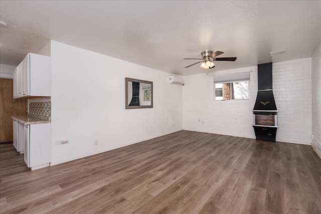 unfurnished living room featuring a wood stove, ceiling fan, an AC wall unit, and wood finished floors