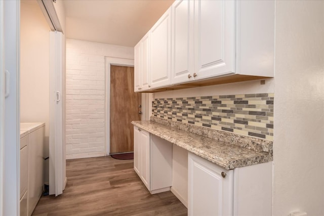 kitchen featuring brick wall, white cabinetry, wood finished floors, backsplash, and washer / dryer