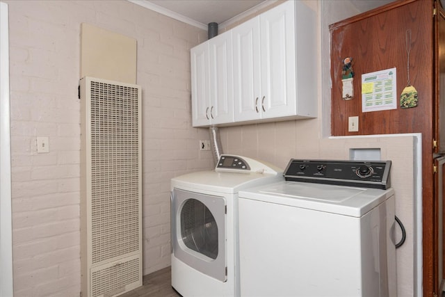 laundry area featuring brick wall, a heating unit, cabinet space, and washer and clothes dryer