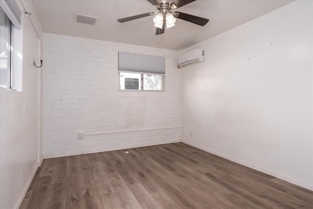 spare room featuring brick wall, a wall mounted AC, visible vents, and wood finished floors