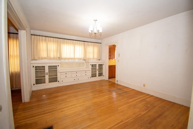 spare room featuring a chandelier, light wood-type flooring, and baseboards