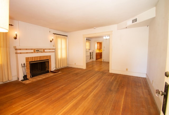 unfurnished living room featuring visible vents, a chandelier, wood finished floors, a brick fireplace, and baseboards