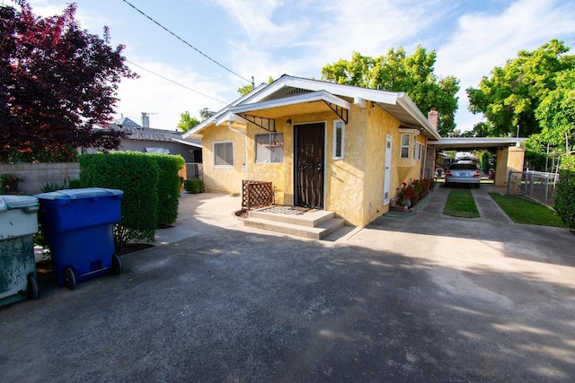 bungalow-style home with fence, an attached carport, driveway, and stucco siding