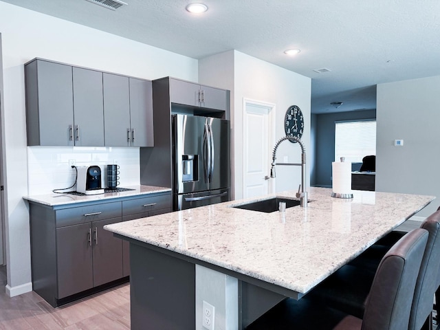 3395 Las Rosas Ave, Clovis, CA 93619 - kitchen with stainless steel fridge with ice dispenser, gray cabinetry, a breakfast bar, light stone countertops, and a kitchen island with sink