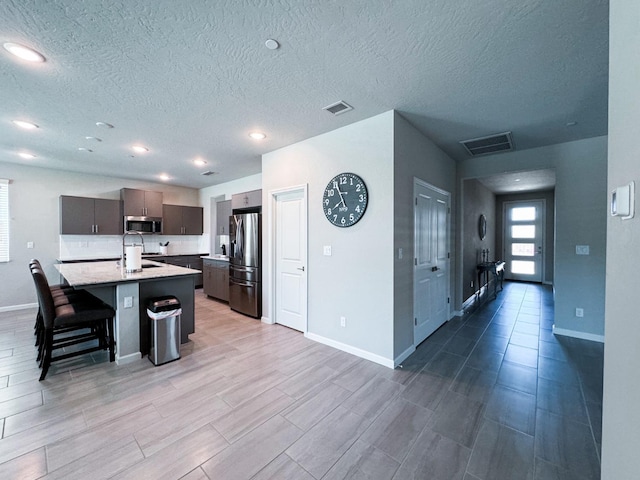 3395 Las Rosas Ave, Clovis, CA 93619 - kitchen featuring stainless steel appliances, light countertops, an island with sink, a breakfast bar area, and a textured ceiling
