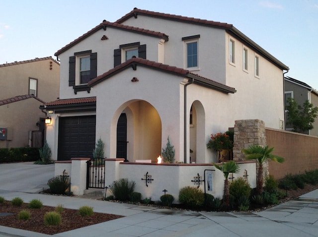 mediterranean / spanish-style house with concrete driveway, stucco siding, an attached garage, a fenced front yard, and a tile roof