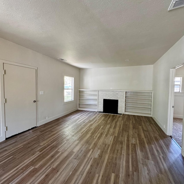 unfurnished living room featuring plenty of natural light, dark wood-type flooring, and a textured ceiling