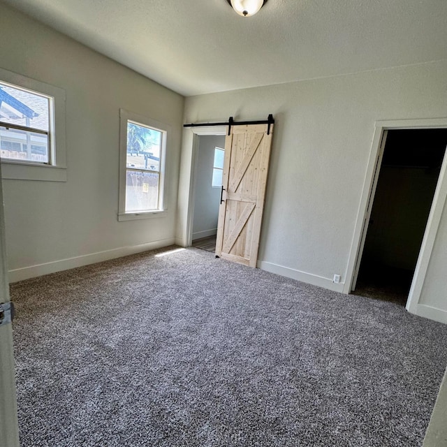 unfurnished bedroom featuring baseboards, multiple windows, carpet flooring, and a barn door