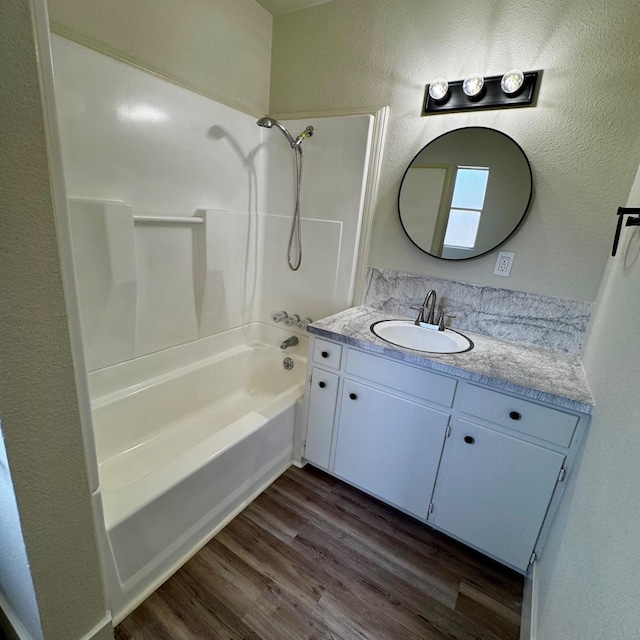 full bathroom with a textured wall, vanity, tub / shower combination, and wood finished floors