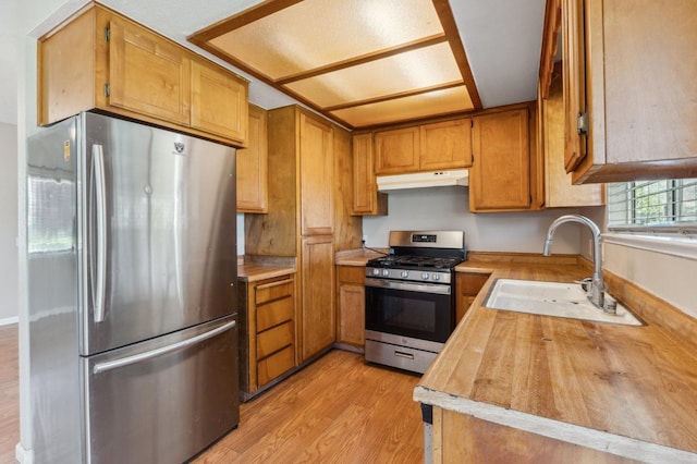 704 Rosehill Dr, Chowchilla, CA 93610 - kitchen with a sink, under cabinet range hood, brown cabinets, light wood finished floors, and stainless steel appliances