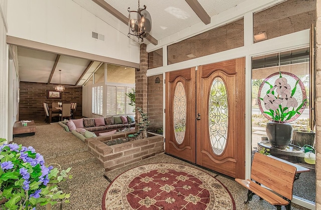foyer entrance with high vaulted ceiling, beamed ceiling, visible vents, a chandelier, and brick wall