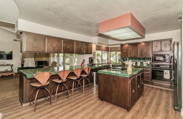 kitchen with dark brown cabinets, black appliances, and tile countertops