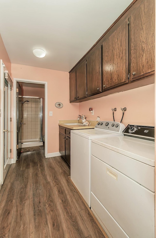 clothes washing area with dark wood finished floors, separate washer and dryer, a sink, baseboards, and cabinet space