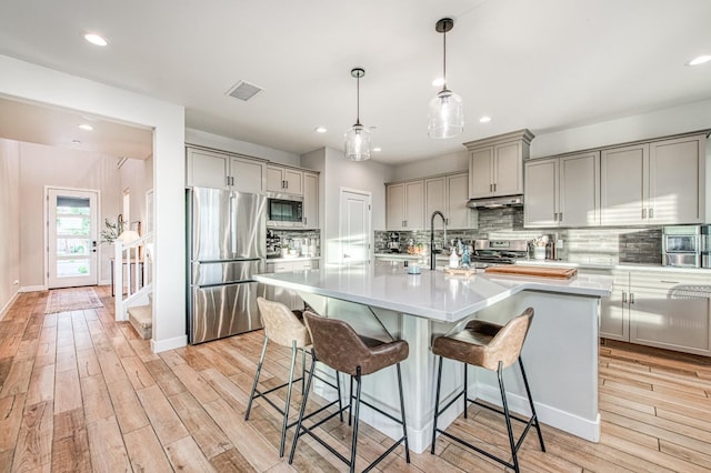 kitchen featuring light wood-style flooring, a kitchen bar, gray cabinets, light countertops, and appliances with stainless steel finishes