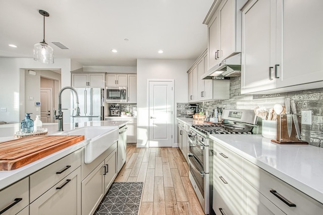kitchen with light wood-style floors, backsplash, under cabinet range hood, light countertops, and appliances with stainless steel finishes