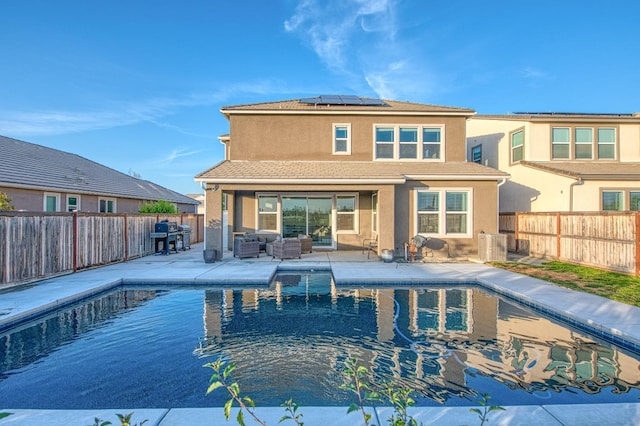 rear view of house with stucco siding, a fenced backyard, solar panels, a fenced in pool, and an outdoor hangout area