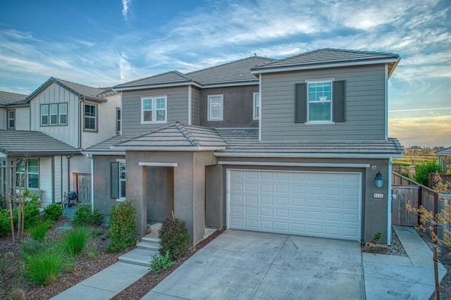 view of front of property featuring an attached garage, a tiled roof, stucco siding, fence, and concrete driveway