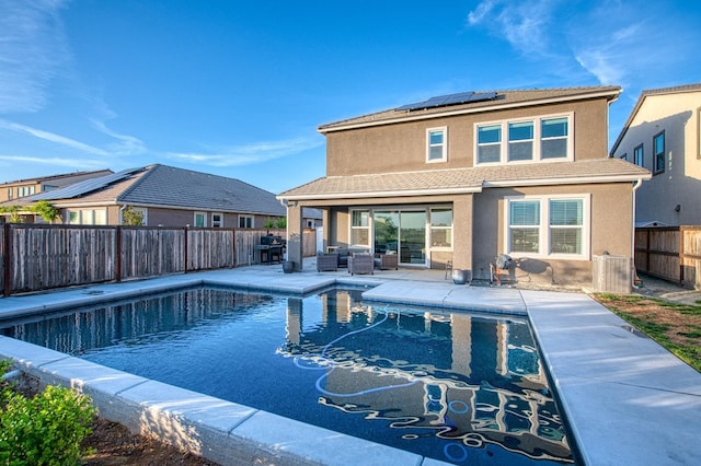 back of house featuring a patio area, a fenced backyard, roof mounted solar panels, a fenced in pool, and an outdoor hangout area