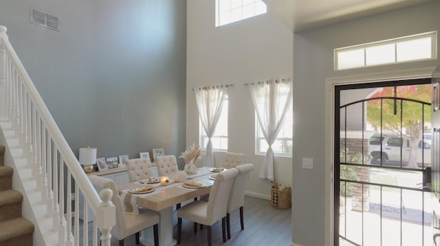 dining space featuring stairway, visible vents, a high ceiling, and wood finished floors