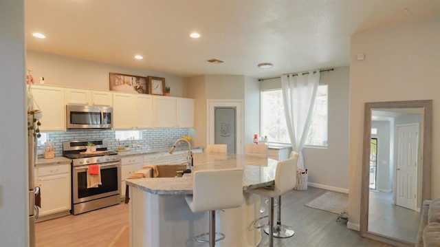kitchen featuring light wood-style flooring, white cabinetry, visible vents, decorative backsplash, and appliances with stainless steel finishes