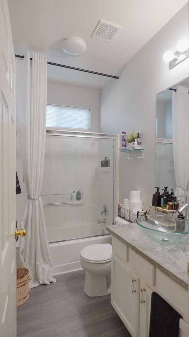full bath featuring combined bath / shower with glass door, visible vents, toilet, and wood finished floors