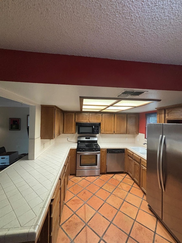 1225 Pontiac Ave, Clovis, CA 93612 - kitchen with appliances with stainless steel finishes, tile countertops, brown cabinets, a textured ceiling, and light tile patterned floors
