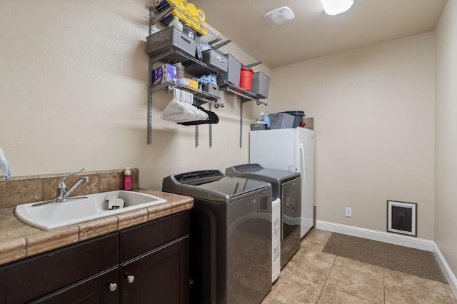 laundry room with a sink, cabinet space, washer and clothes dryer, light tile patterned flooring, and baseboards