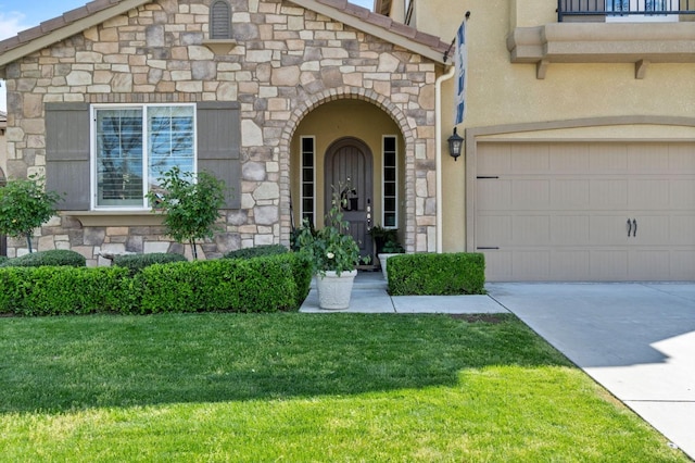 doorway to property featuring stucco siding, driveway, a lawn, and stone siding
