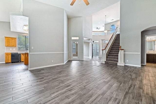 4650 W Roberts Ave, Fresno, CA 93722 - unfurnished living room featuring ceiling fan, dark wood-style flooring, a towering ceiling, stairs, and arched walkways
