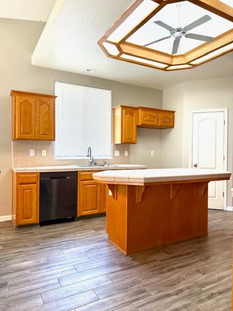4650 W Roberts Ave, Fresno, CA 93722 - kitchen with black dishwasher, tile counters, a sink, wood finished floors, and backsplash