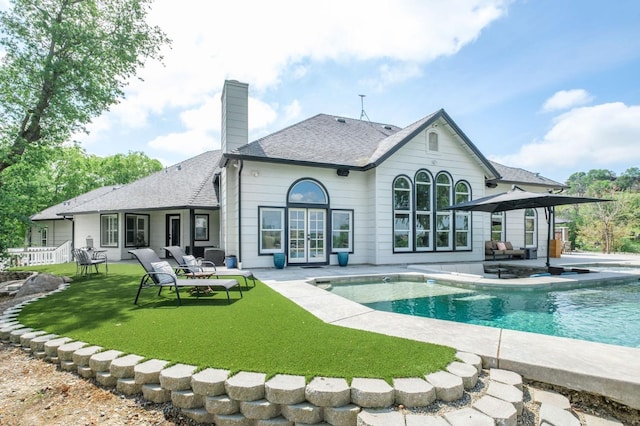rear view of house featuring roof with shingles, an outdoor pool, a chimney, a lawn, and a patio