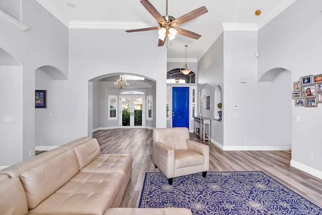 living area with a high ceiling, crown molding, arched walkways, ceiling fan with notable chandelier, and wood finished floors