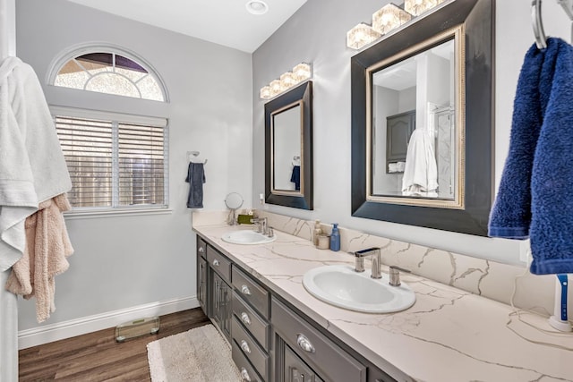 full bath with a sink, baseboards, double vanity, and wood finished floors